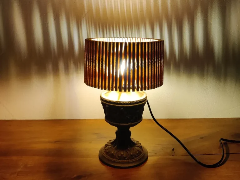 Die eingeschaltete Unikat-Lampe aus Altholz und Metallfuß erzeugt durch ihren Lamellenschirm ein markantes Schattenspiel