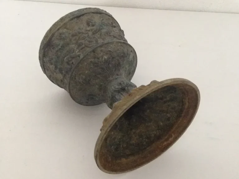 Originalzustand des Lampenfußes: Ein historischer Kelch aus Metall mit sichtbarer Alterung und figürlichen Reliefs.
